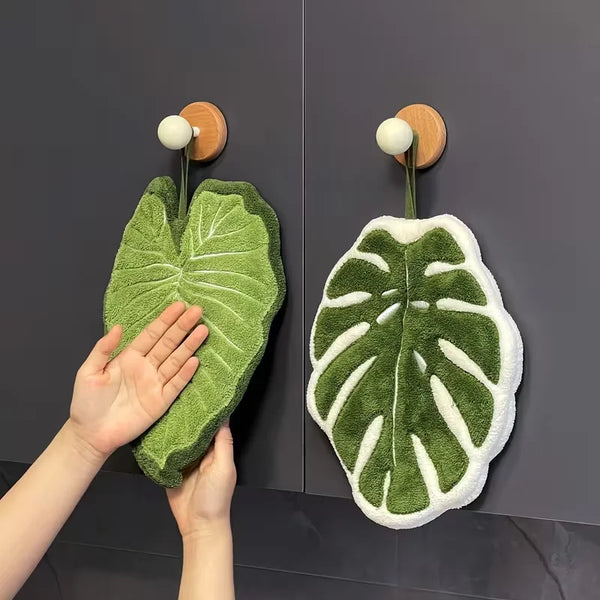 A hand is holding a green leaf-shaped absorbent microfiber towel against a dark gray background.