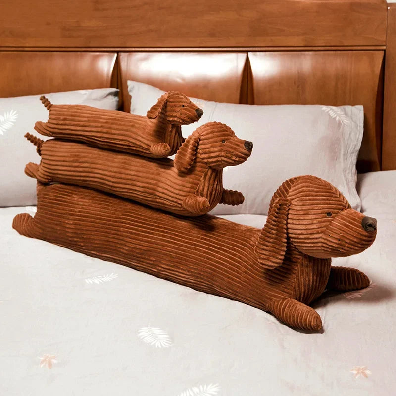 A set of three brown corduroy dachshund dog body pillows resting on a white bed.