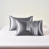 A set of two smooth, metallic silver satin pillowcases resting on a white surface.