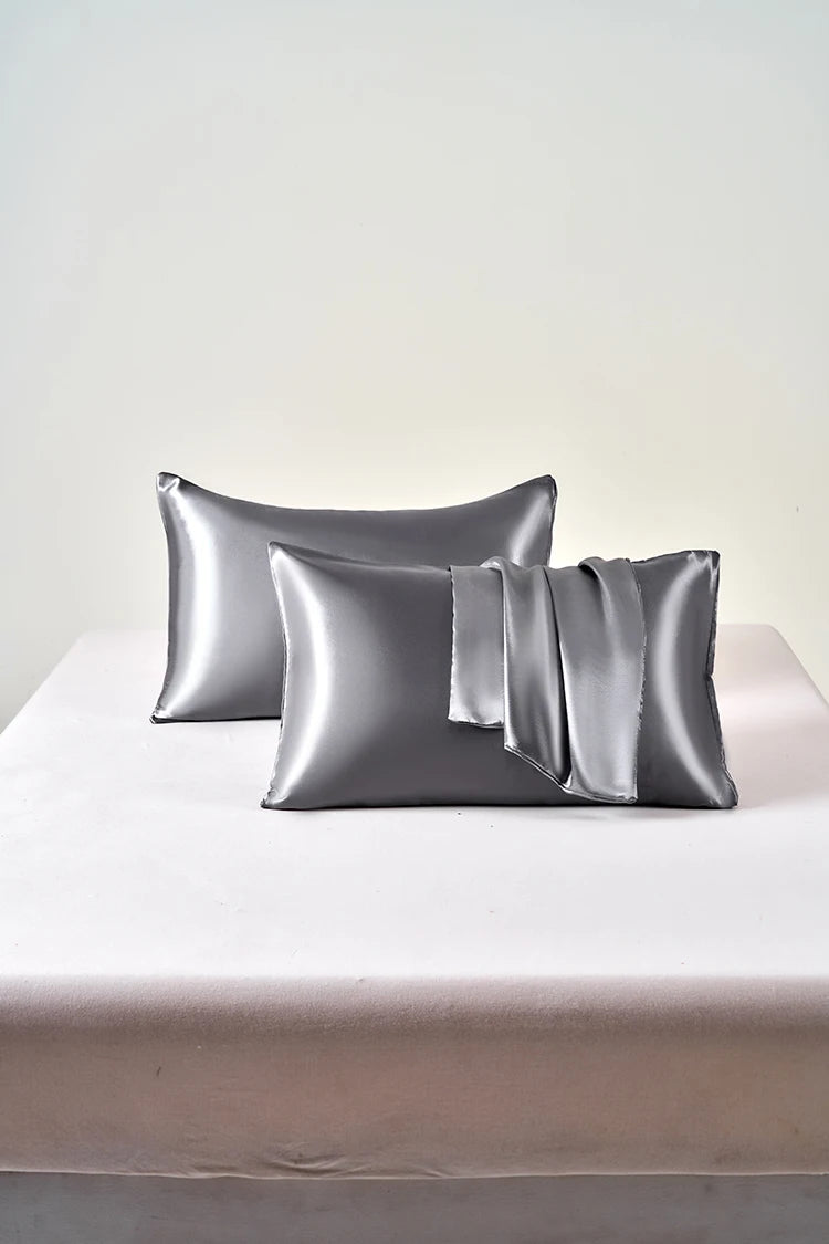 A set of two smooth, metallic silver satin pillowcases resting on a white surface.