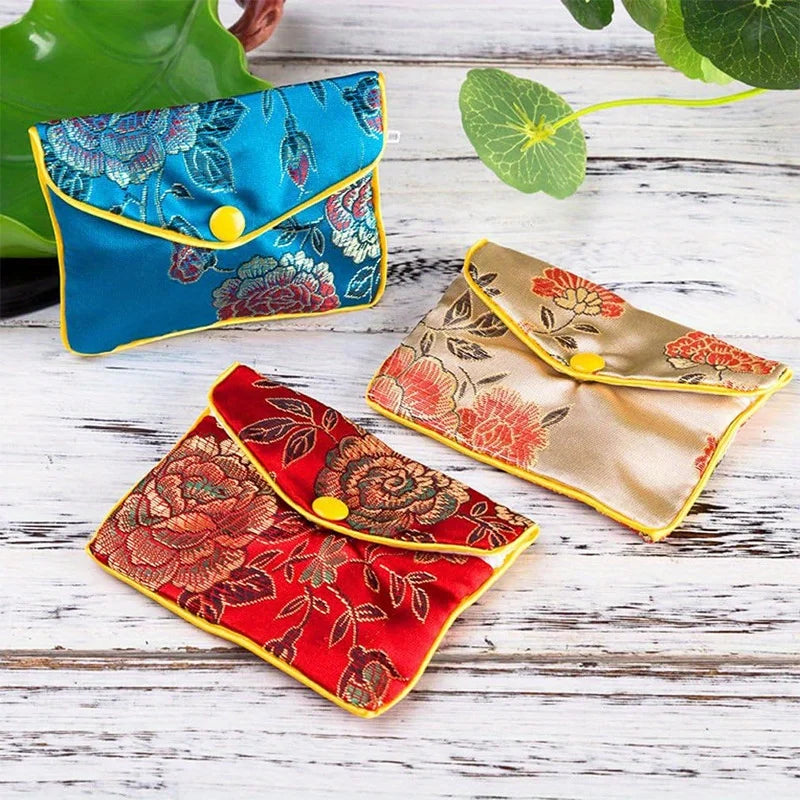 Three silk brocade jewelry pouches in blue, red, and gold accents are displayed on a white wooden surface.