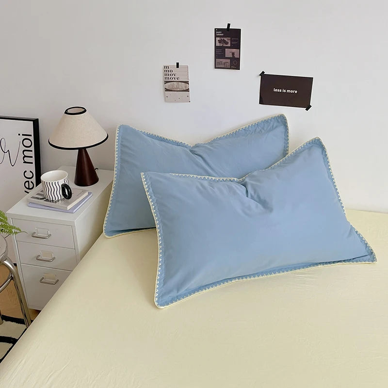 A light blue bed linen set featuring four pillows and a matching duvet on a cream-colored bed.