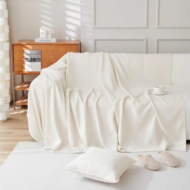 A cream solid color anti-scratch sofa cover draped over a white sofa with a white pillow on a light floor.