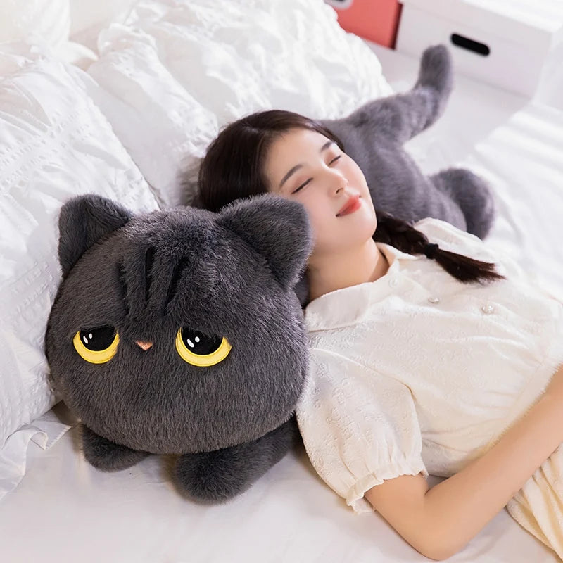 A woman is resting her head on a gray cat plush pillow in a bright, white setting.