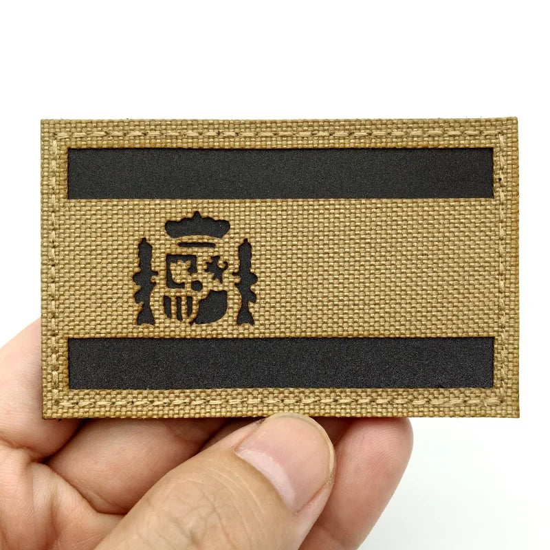 A rectangular tactical patch featuring a woven gold fabric with black stripes and an emblem.