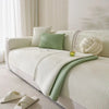 A light green machine washable anti-slip sofa slipcover with cream pillows and a white knitted throw on a modern sofa.