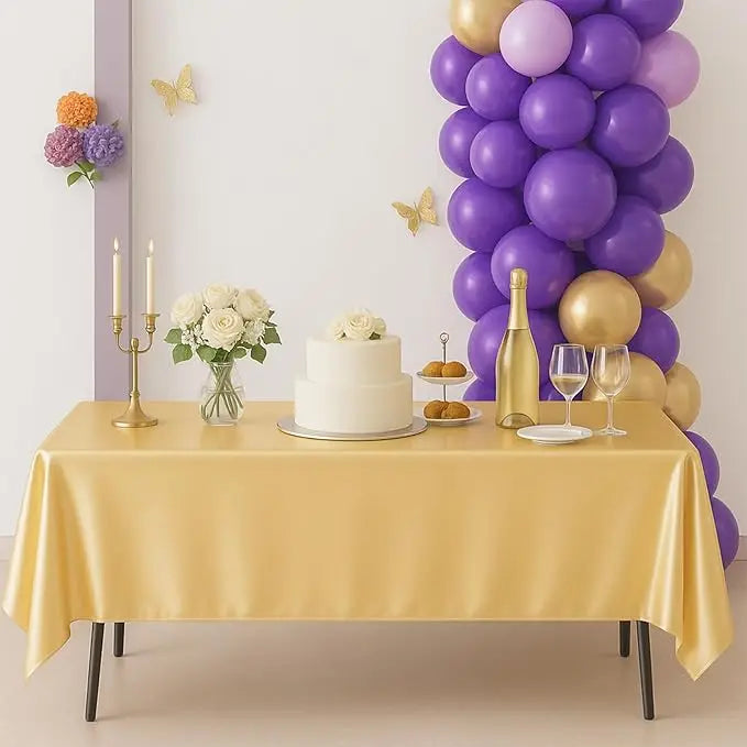 A gold satin tablecloth is set for an elegant dining or party decor display with a white cake and balloons.