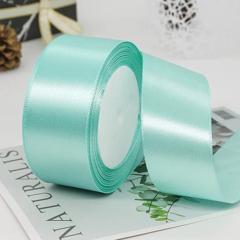 Roll of mint green satin craft ribbon with decorative trim shown on a white surface.