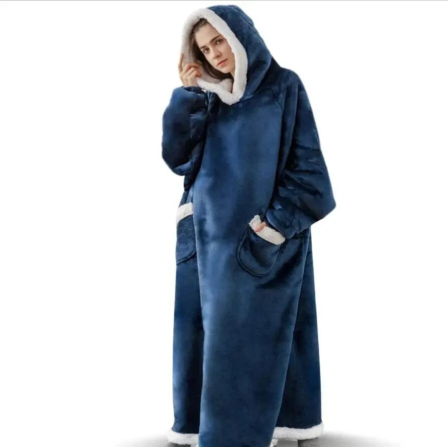 A person wearing a dark blue velvet oversized flannel blanket pyjama set with a white hood and pocket details.