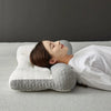 A person is lying down using a gray 3D ergonomic contour pillow for neck and spine support.