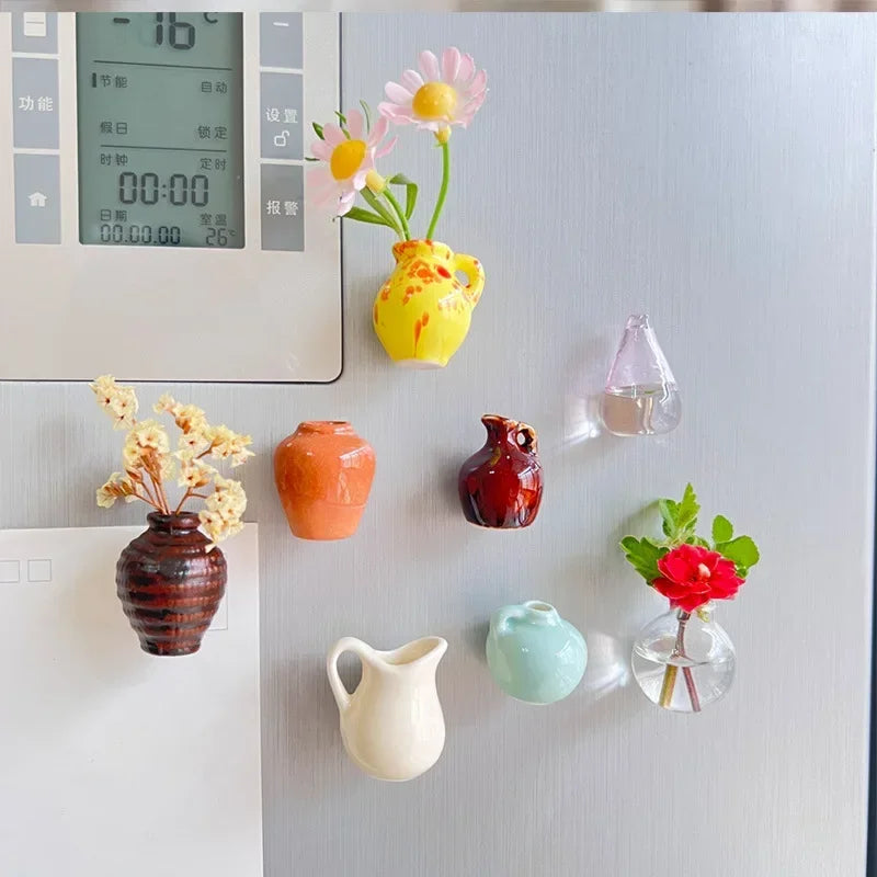 A collection of colorful mini ceramic landscape magnets, including flowers and vessels, displayed on a refrigerator.