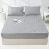 A gray waterproof mattress and bed protector sheet is shown on a mattress, with water droplets visible on the surface.