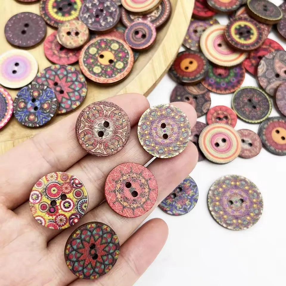 A hand holds various vintage wooden buttons in shades of pink, purple, and green on a light wooden surface.