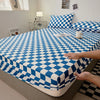 A blue and white checkered fitted sheet is being handled on a bed, with pillows and decorative items visible in the backgroun