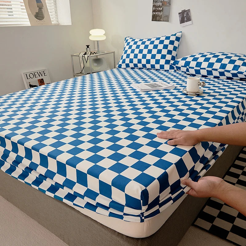 A blue and white checkered fitted sheet is being handled on a bed, with pillows and decorative items visible in the backgroun