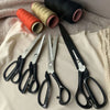A collection of professional heavy duty fabric scissors in various colors and materials laid on a light fabric background.