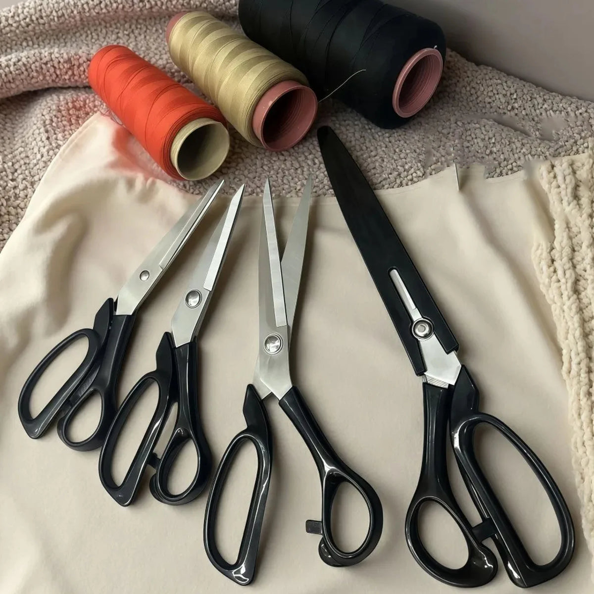 A collection of professional heavy duty fabric scissors in various colors and materials laid on a light fabric background.
