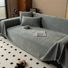 A minimalist gray chenille sofa cover draped over a sofa with throw pillows and a small decorative item.