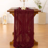 A deep burgundy cheesecloth table runner draped over a wooden table, decorated with white flowers.