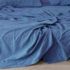 A soft blue pure linen flat sheet draped on a bed, showing its texture and folds.