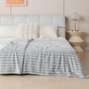 A soft gray flannel throw blanket draped over a bed with white pillows and a bedside lamp.
