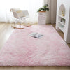 A pink shaggy rug is displayed on a wooden floor next to a white chair and a potted plant.
