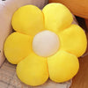 A bright yellow sunflower plush flower cushion resting on a textured fabric surface.