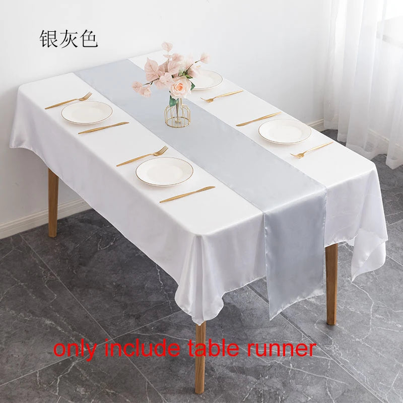 A white satin table runner set for dining featuring gold cutlery and pink floral accents on a wooden table.