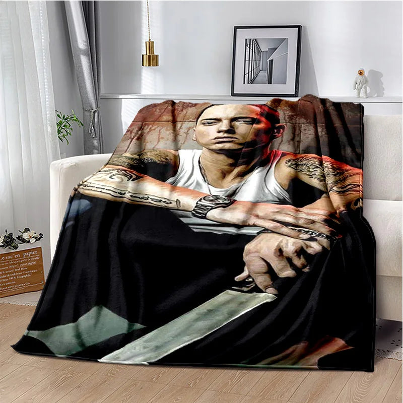 A dark graphic throw blanket featuring a portrait of a man with tattoos and a knife, draped over a white sofa.