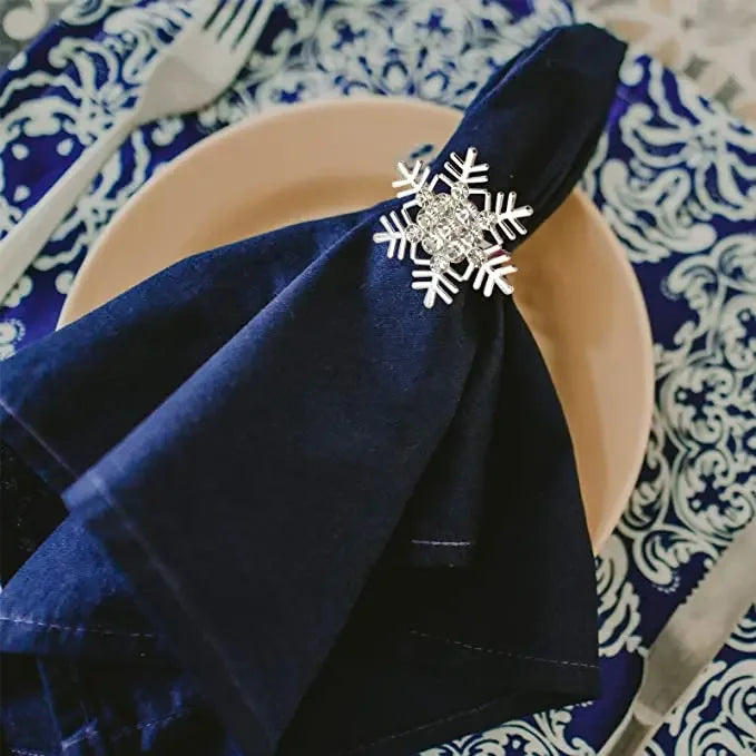 A dark blue velvet napkin tied with a silver snowflake ring placed on a light pink plate set against a blue and white pattern