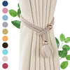 A close-up of a beige curtain with decorative rope tiebacks and pearl-colored fabric accents.
