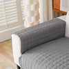 A gray quilted anti-slip sofa cover with a plush texture displayed on a white sofa.