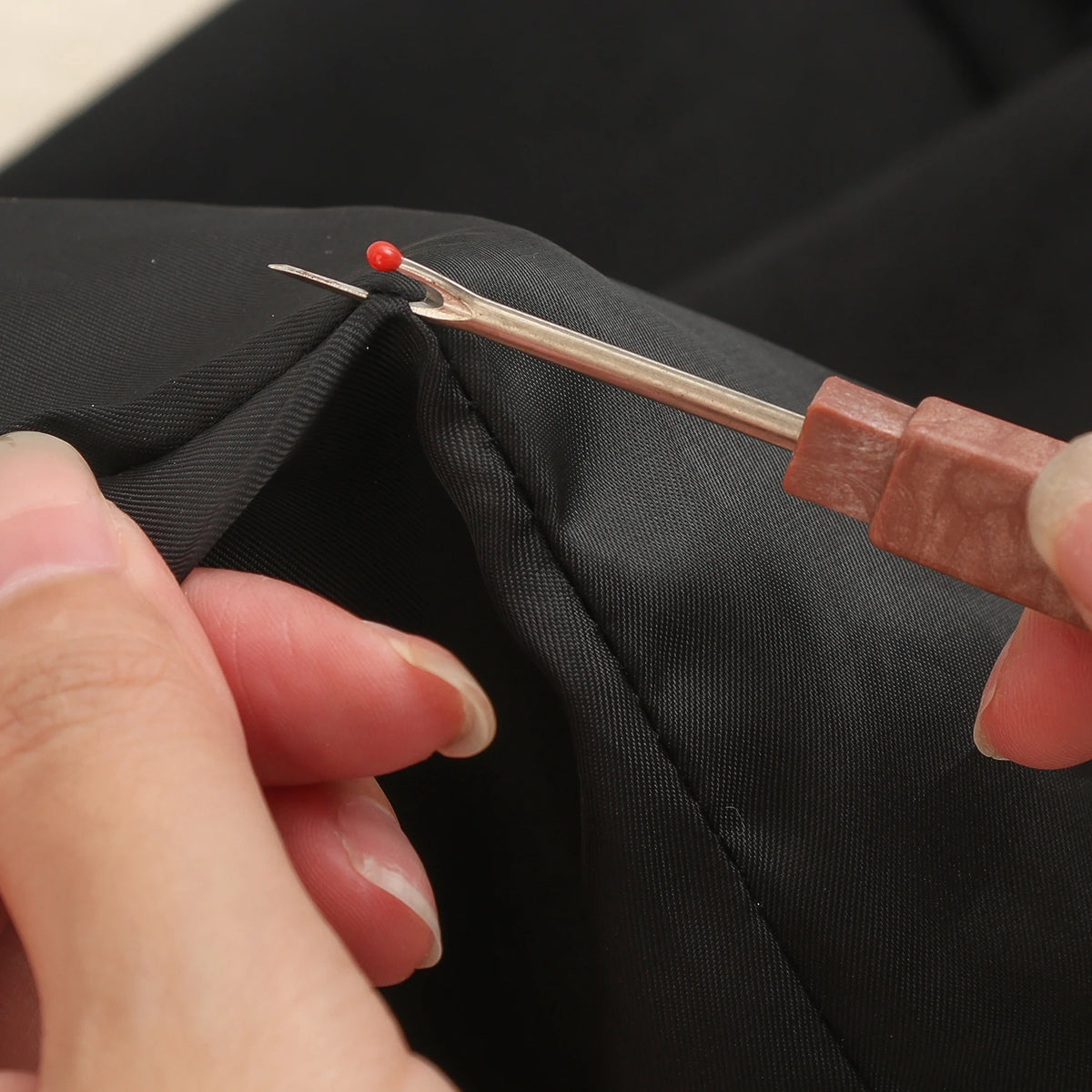 A hand is using a portable sewing needle kit to thread a red needle through fabric.