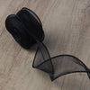 A roll of black wavy edge organza ribbon lying on a wooden surface.