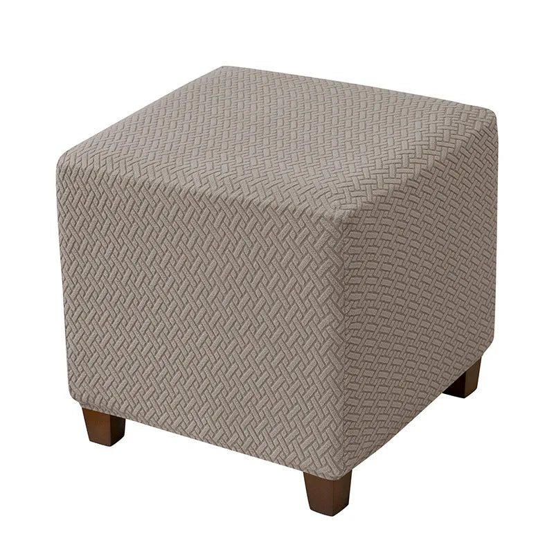 A square ottoman slipcover in a light taupe color with a diamond pattern.