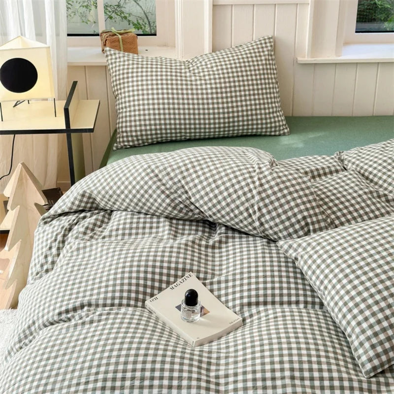 A set of three plaid duvet covers and pillowcases in olive green and white gingham pattern displayed on a bed.