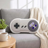 A white gamer controller plush toy resting on a gray sofa next to a cream-colored throw blanket.