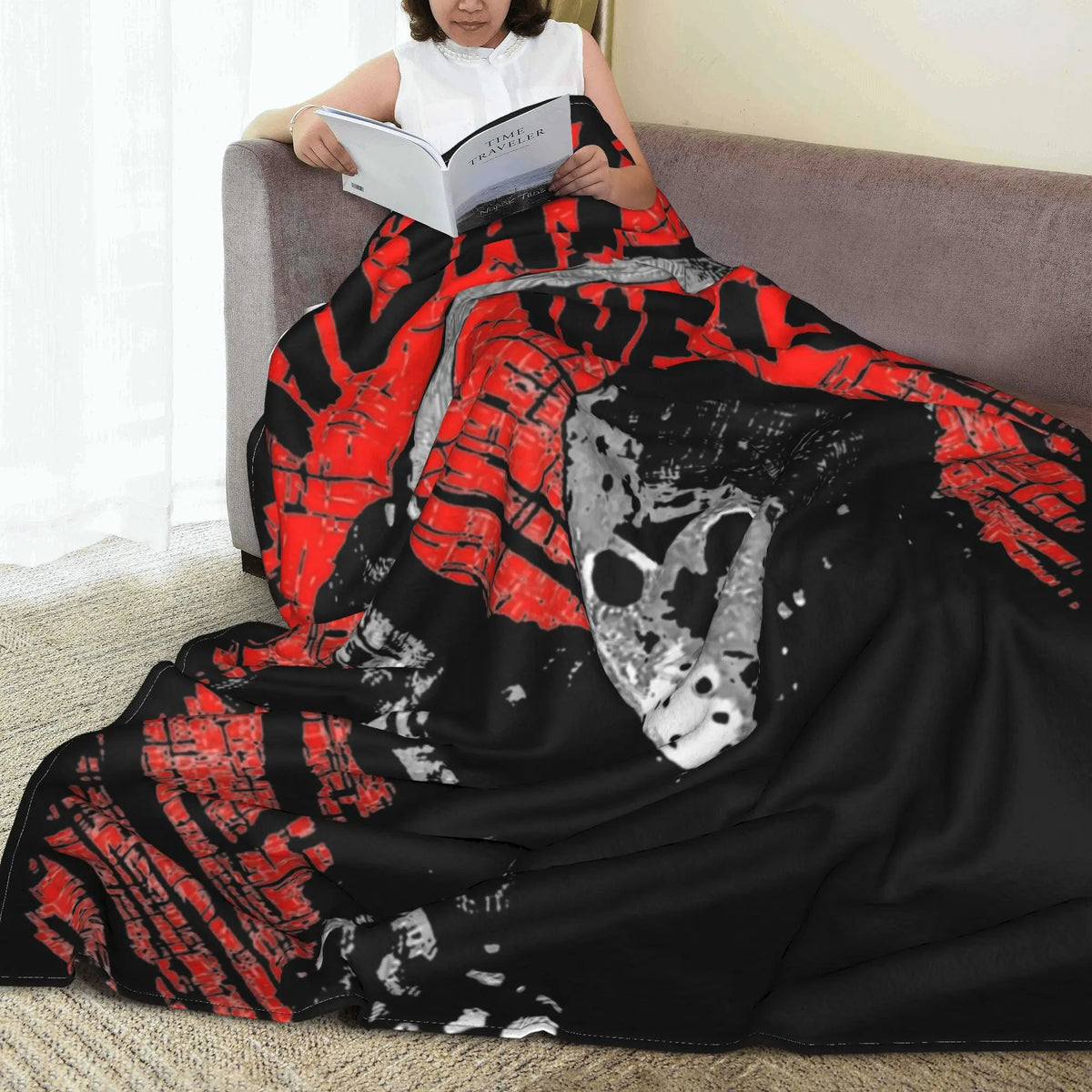 A black and red horror movie themed fleece throw blanket draped over a person reading a book.