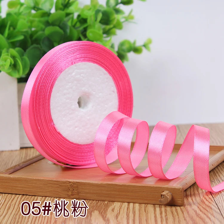 Pink satin ribbon roll with a pink core displayed on a wooden surface.
