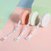 Three retractable double-sided measurement tapes in pink, light green, and white are displayed on a pink surface.