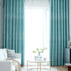 Light blue sheer curtains frame a window with heavy teal blackout drapes and a gold accent rug.