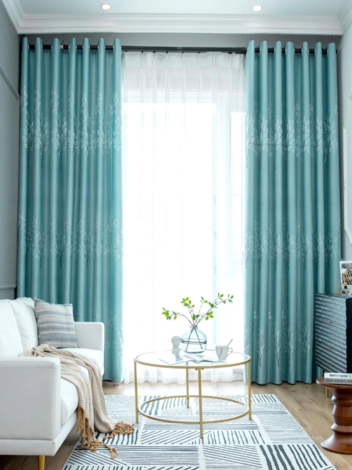 Light blue sheer curtains frame a window with heavy teal blackout drapes and a gold accent rug.