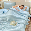 A woman is relaxing under a light blue breathable waffle quilt in a bright room.