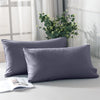 Two solid gray microfiber pillow covers displayed on a white surface with greenery in the background.