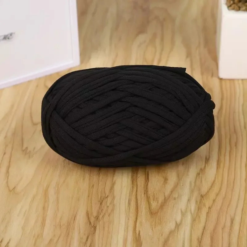 A coil of black flat thread yarn for crafting and sewing lying on a wooden surface.
