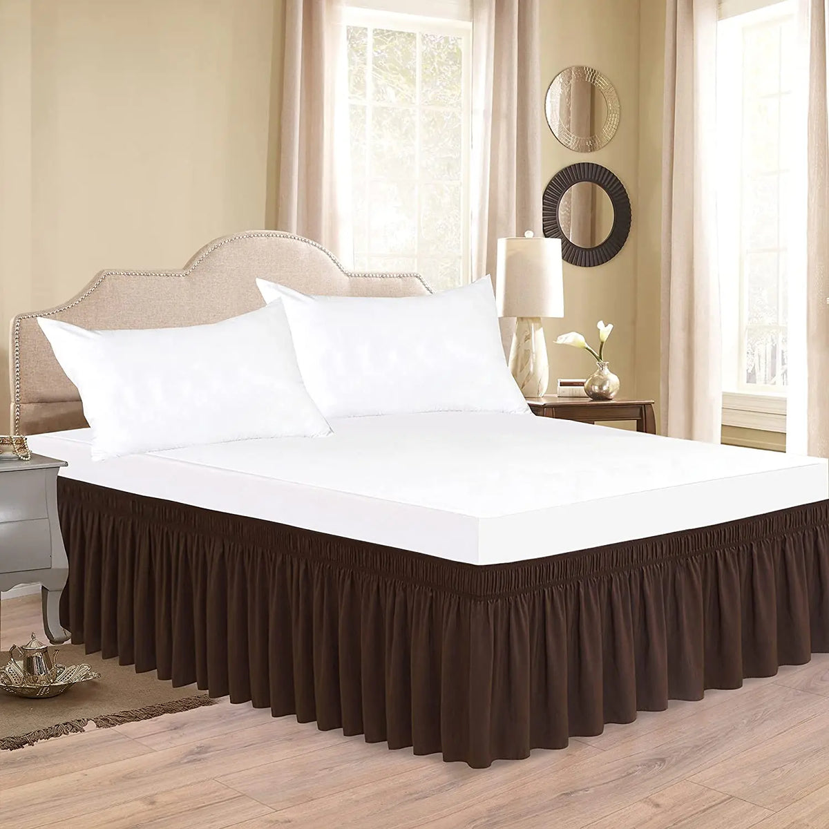 A white bed with a dark brown ruffle skirt and white pillows in a bright bedroom setting.