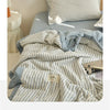 A striped light gray and white luxury jacquard quilt draped on a bed, with a pillow nearby.