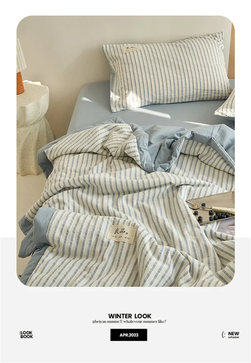A striped light gray and white luxury jacquard quilt draped on a bed, with a pillow nearby.