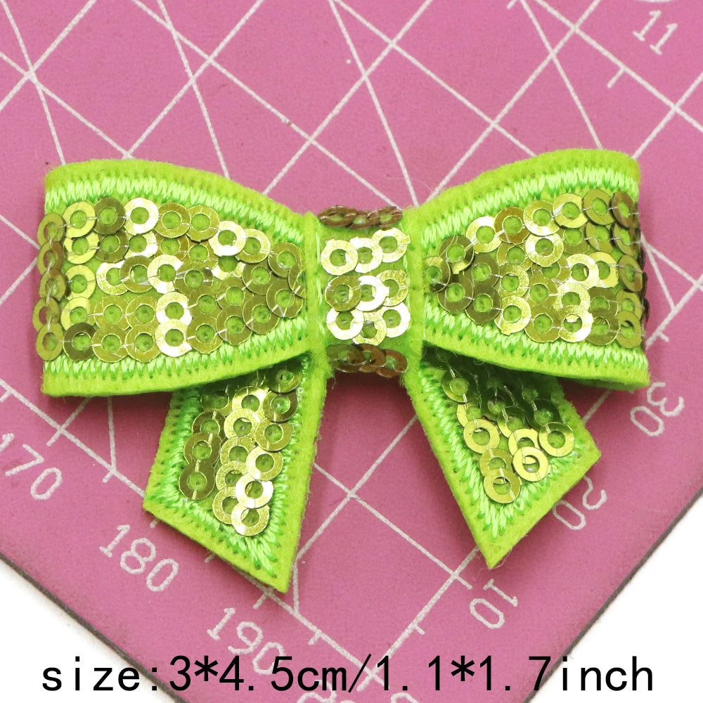 Green sequin bow patches for DIY decoration shown on a pink grid background