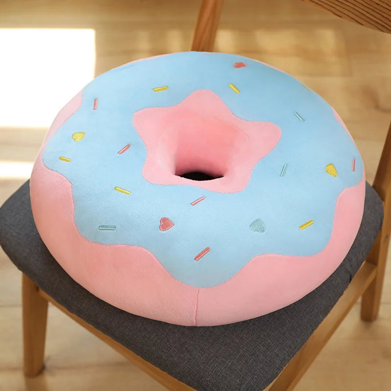 A pink and blue kawaii fried doughnut plush pillow with sprinkles resting on a gray fabric surface.